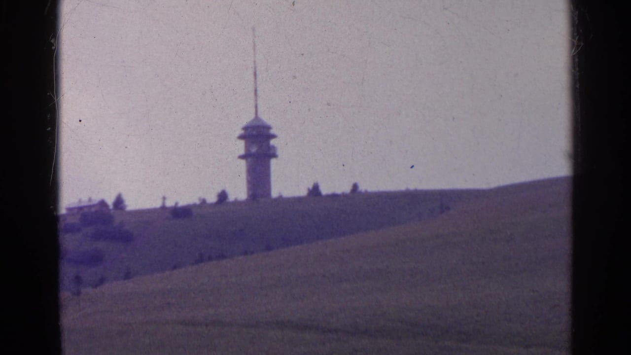 1961 Switzerland home-movie frame showing a slender distant tower on a hill with rolling green fields and sparse trees.