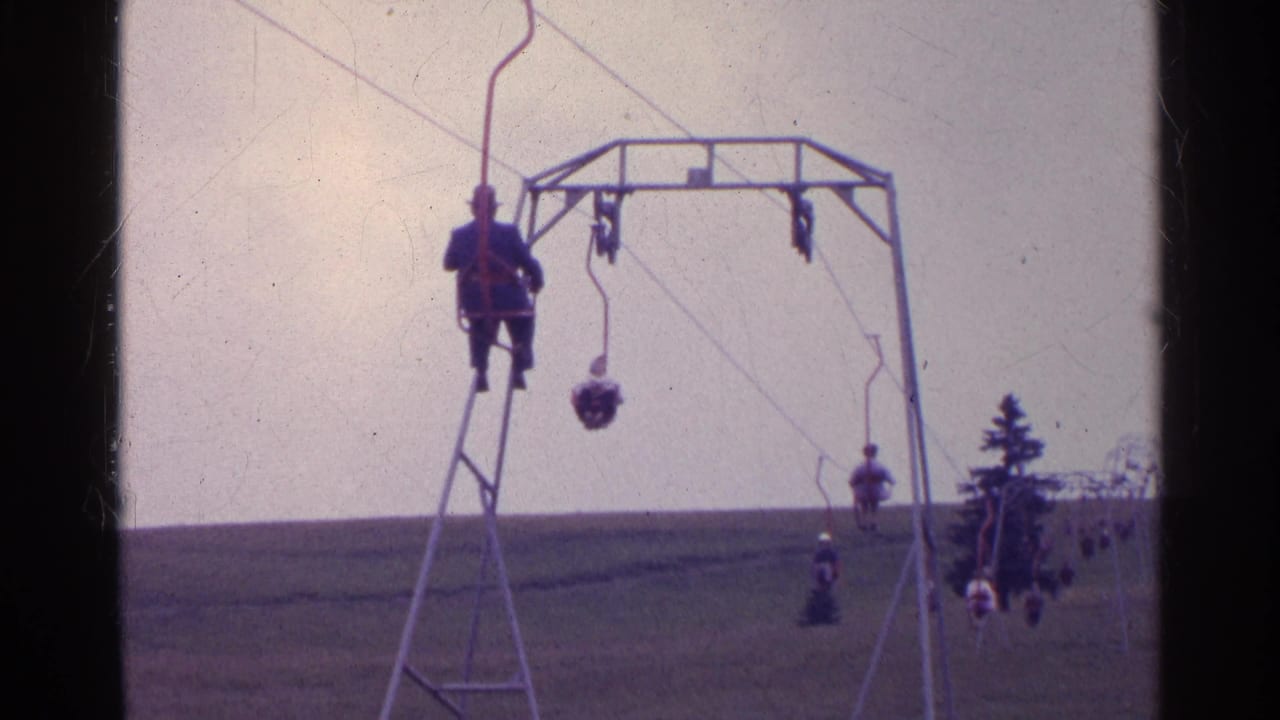 1961 Switzerland frame with multiple ski-lift chairs, a metal tower, distant riders, and evergreens at the edge of the slope.