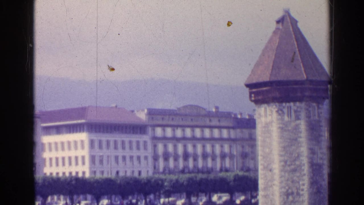 Swiss town view with a historic stone tower, pale civic buildings, and hazy mountains in the background.
