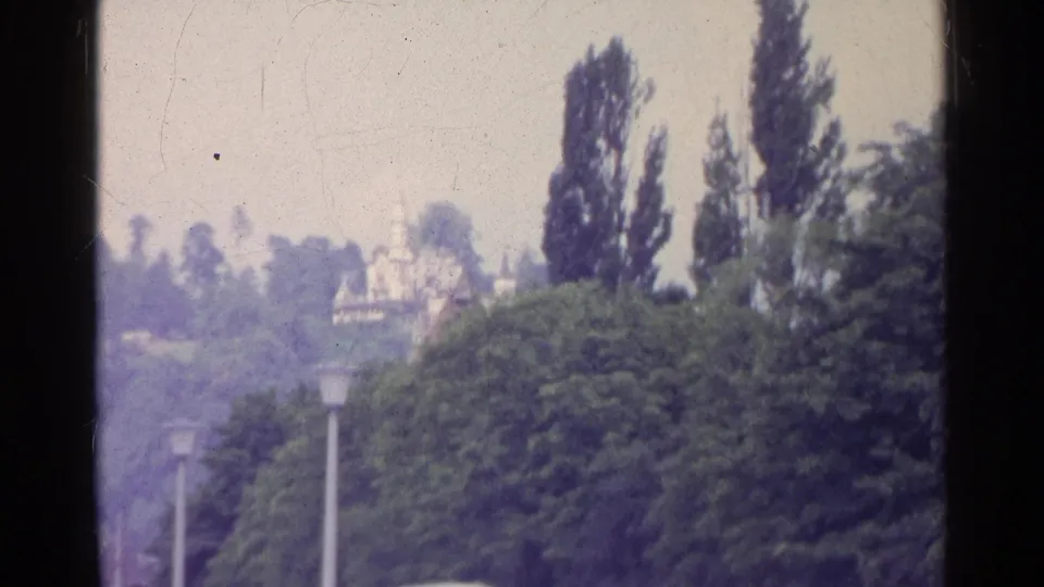 1961 Switzerland frame with trees, street lamps, distant cars, and a pale building seen through soft 8mm color fading.