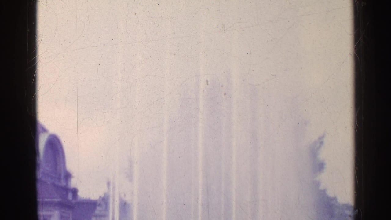 1961 Swiss 8mm frame showing pale fountain jets rising beside a partly visible arched public building.