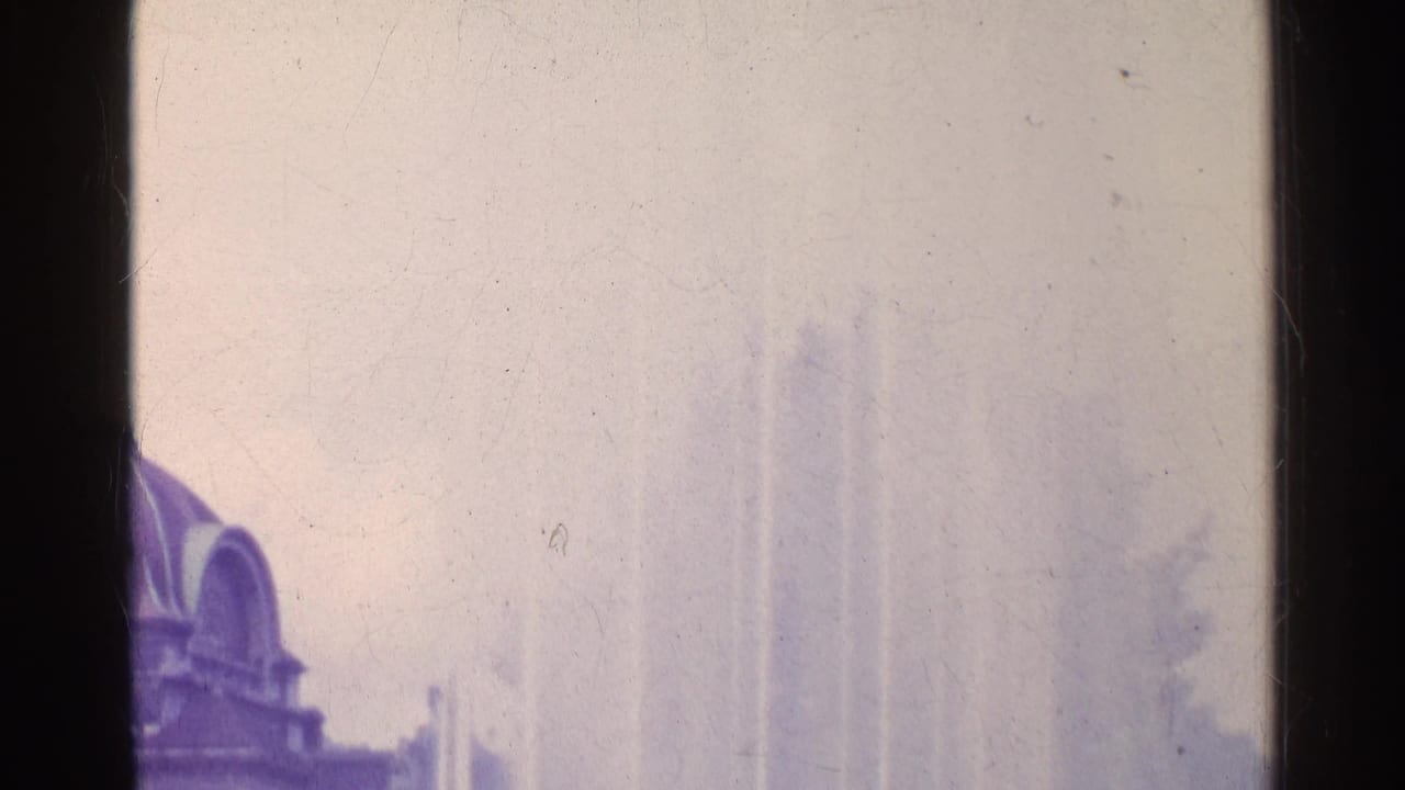 1961 travel footage frame showing a fountain plume and partial brown arched building in Switzerland.
