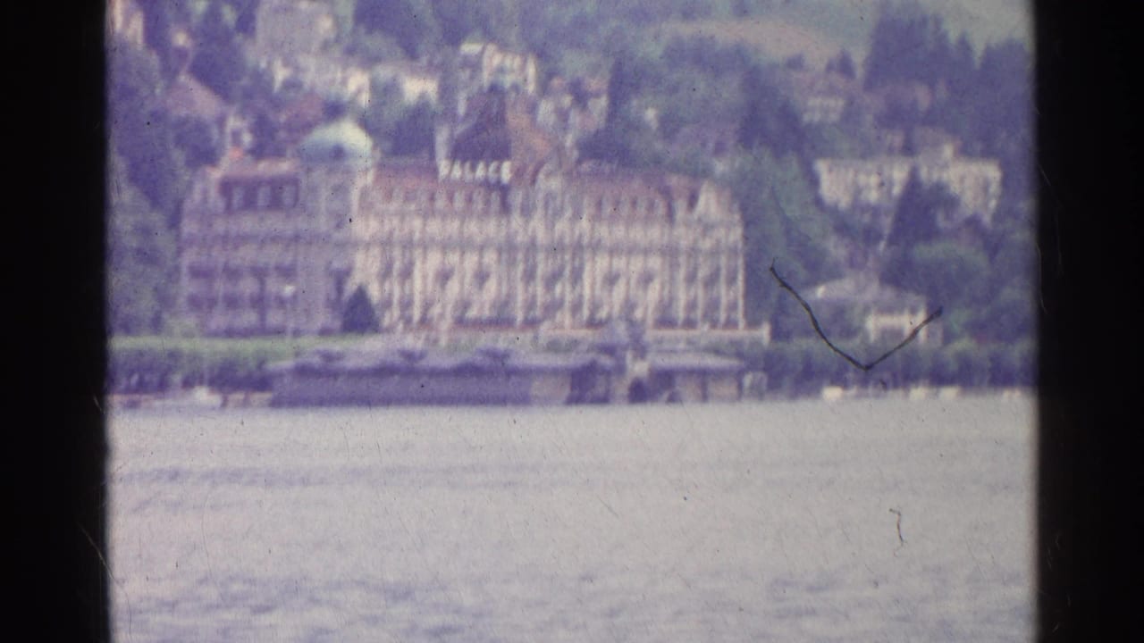 1961 Swiss lakeside view showing a large hotel marked PALACE, water in the foreground, and a wooded hillside town behind.
