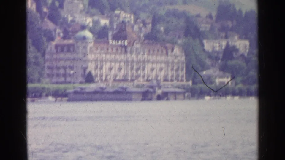 1961 Swiss lakeside view showing a large hotel marked PALACE, water in the foreground, and a wooded hillside town behind.