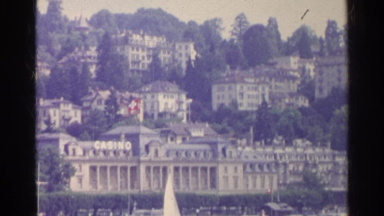 1961 Switzerland home-movie frame with casino signage, lakefront architecture, wooded hillside, and resort buildings above.