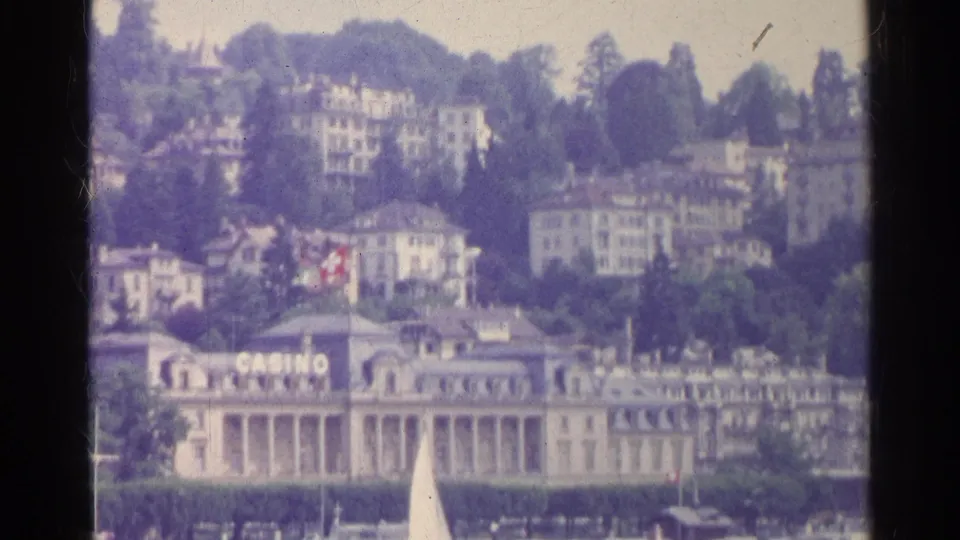 1961 Switzerland home-movie frame with casino signage, lakefront architecture, wooded hillside, and resort buildings above.