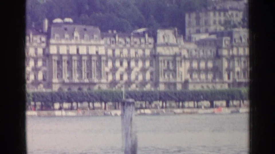 Distant Swiss lakeside buildings and trees appear across the water in a soft 1961 8mm travel frame.