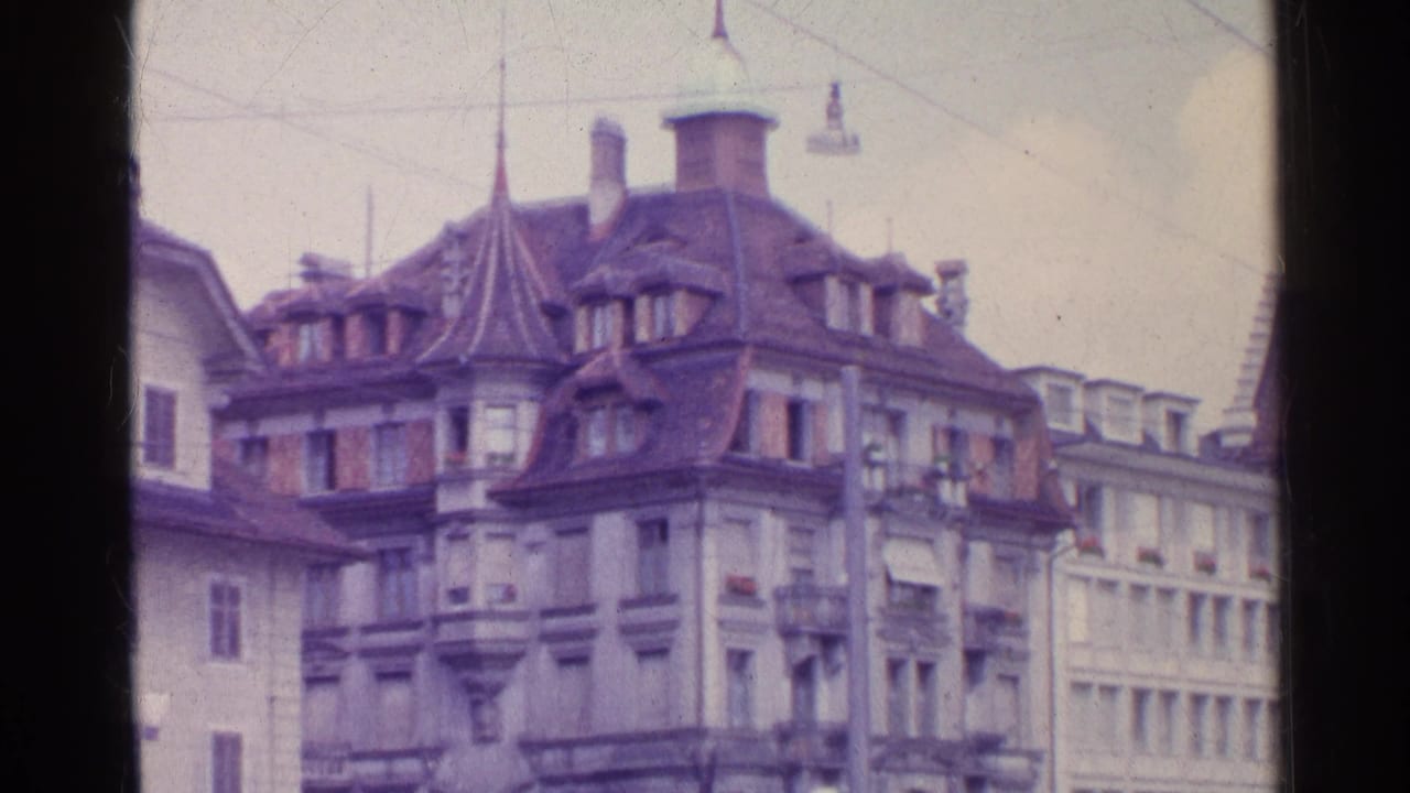 1961 Swiss street view with steep-roofed historic buildings, dormer windows, overhead wires, and neighboring facades.