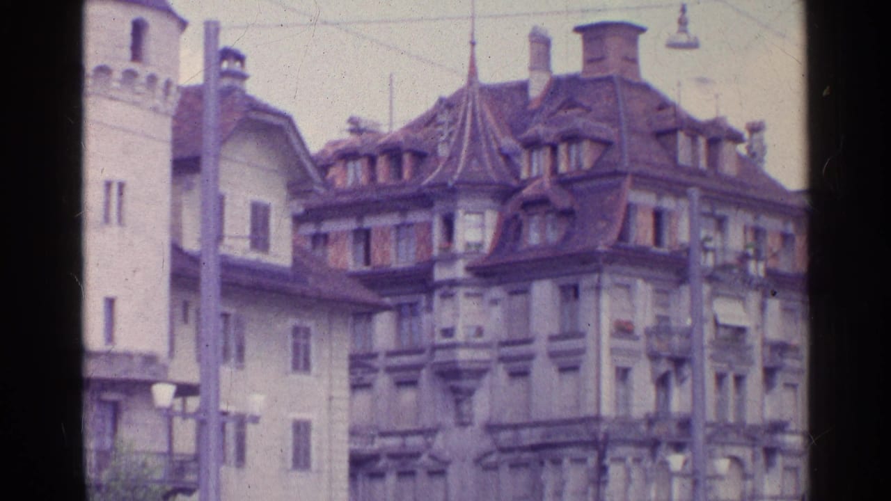 1961 Switzerland 8mm frame showing a stone tower next to historic urban buildings with steep roofs, dormers, and balconies.