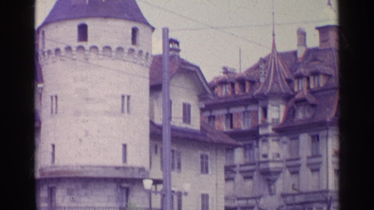 1961 Switzerland 8mm view of a round stone tower with crenellations and neighboring buildings with steep roofs and dormers.