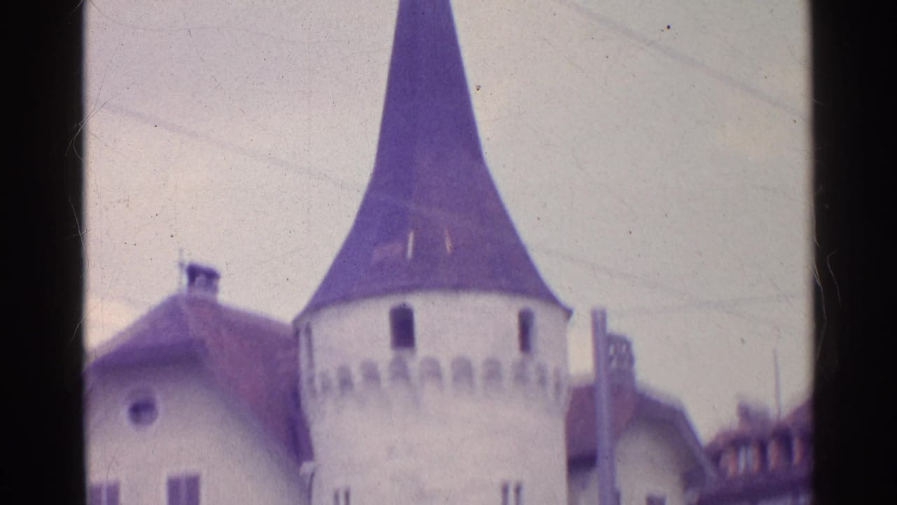 1961 Switzerland 8mm frame centered on a conical-roof stone tower with crenellated detail and nearby historic buildings.