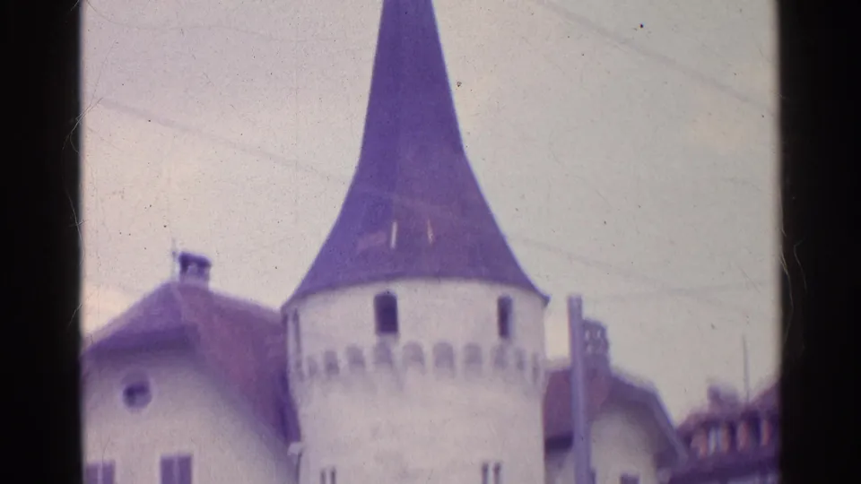 1961 Switzerland 8mm frame centered on a conical-roof stone tower with crenellated detail and nearby historic buildings.