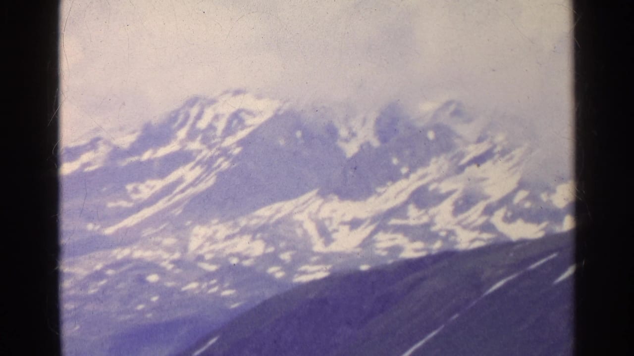 Distant Swiss alpine peaks fill the frame in faded 8mm color, with snowfields, dark slopes, and visible film-frame borders.