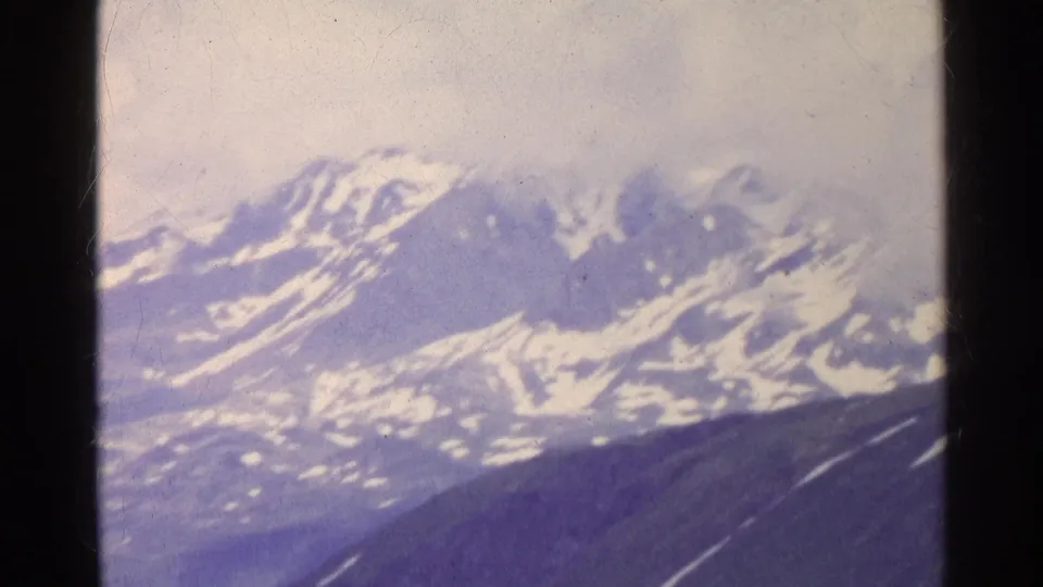 Distant Swiss alpine peaks fill the frame in faded 8mm color, with snowfields, dark slopes, and visible film-frame borders.