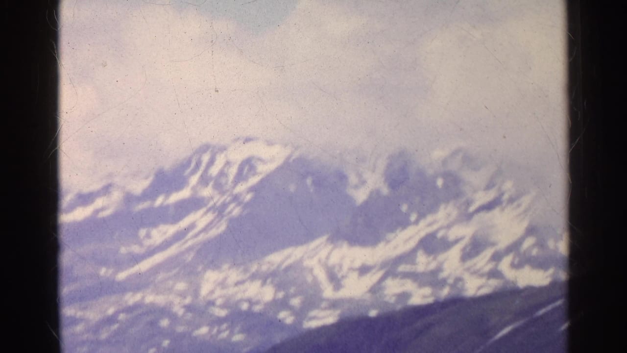 Final 1961 Switzerland frame showing snow-capped alpine mountains, dark foreground slopes, overcast sky, and aged 8mm frame markings.