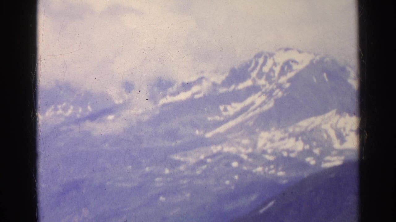 Distant Swiss mountain peaks with snow streaks and low clouds, captured in soft blue-purple 8mm color.