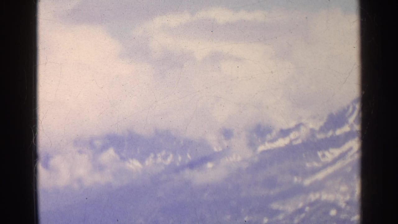Soft 8mm frame of Swiss alpine slopes partly obscured by clouds, with snow patches visible along the ridge.
