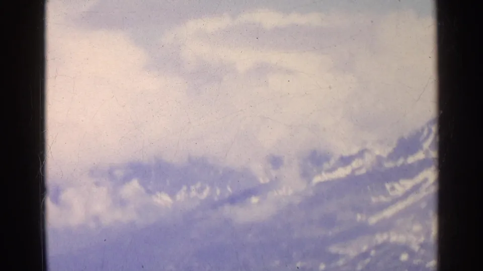Soft 8mm frame of Swiss alpine slopes partly obscured by clouds, with snow patches visible along the ridge.