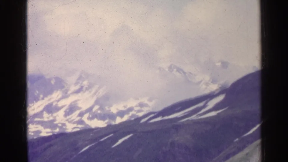 1961 Switzerland 8mm frame with snow-capped mountains and low clouds across the alpine skyline.