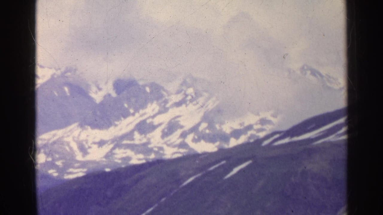 1961 Switzerland 8mm frame showing distant alpine peaks, snow patches, and dark mountain slopes below clouded sky.