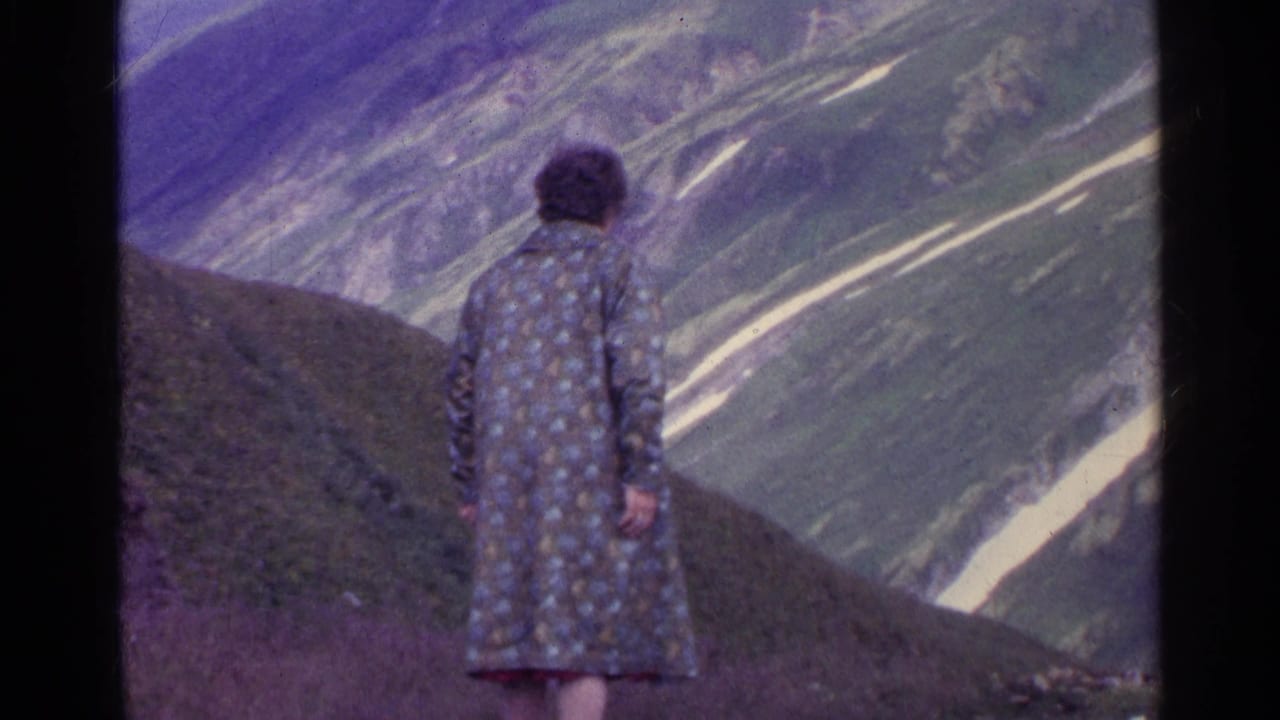 1961 Switzerland 8mm frame with a person seen from behind on a hillside, looking toward snow-streaked mountains.