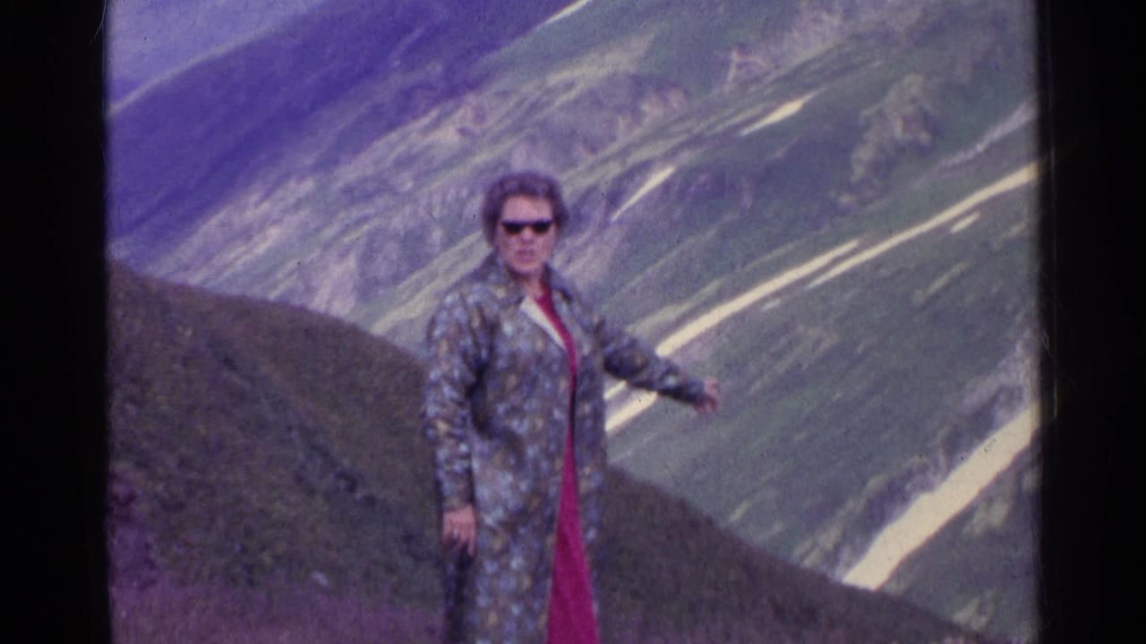 In the 1961 Switzerland home movie, a woman in sunglasses turns toward the camera and points across the alpine view.