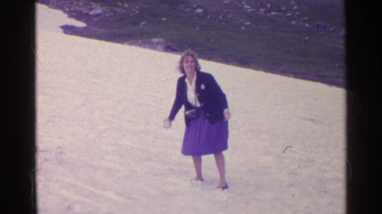 A woman in a dark jacket and purple skirt walks on a snowfield during the 1961 Switzerland mountain trip.