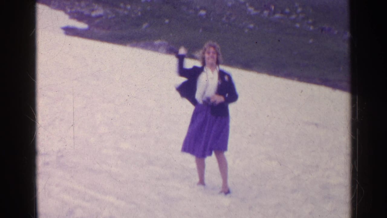 A woman in a dark jacket and purple skirt raises her arm while standing on snow in the 1961 Switzerland footage.