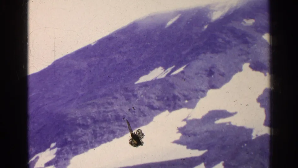 1961 Swiss 8mm frame showing a dark alpine slope with irregular snowfields, pale sky, and aged film borders.