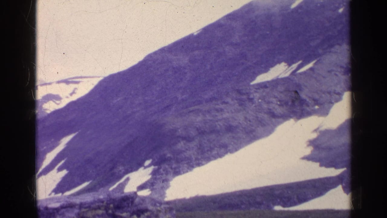 1961 Swiss alpine view with a sloping mountain ridge, scattered snowfields, pale sky, and purple aged-film color.