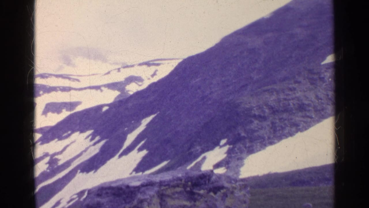 1961 Switzerland home-movie frame of an alpine slope with melting snow patches and a distant snow-covered ridge.