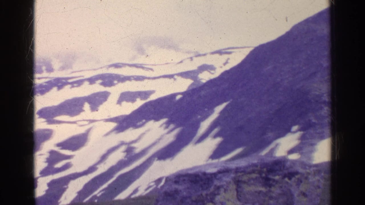 1961 Swiss mountain landscape with layered snowy ridges, dark slope, pale sky, and aged 8mm frame edges.