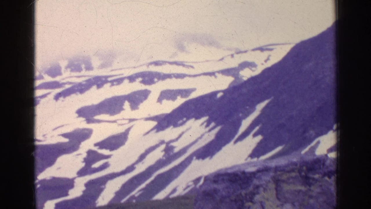 Snow-streaked mountain slopes seen from above with dark film borders.
