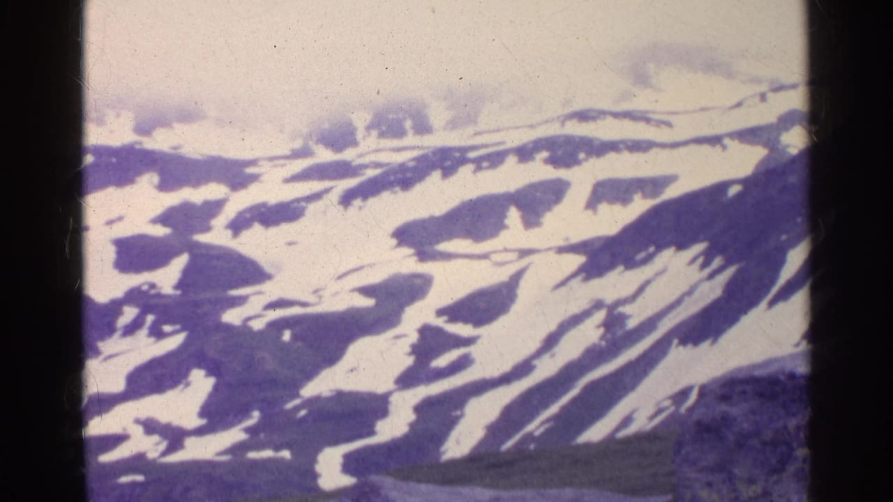 Aerial 8mm view of Swiss alpine ridges with irregular snowfields and soft mid-century color cast.