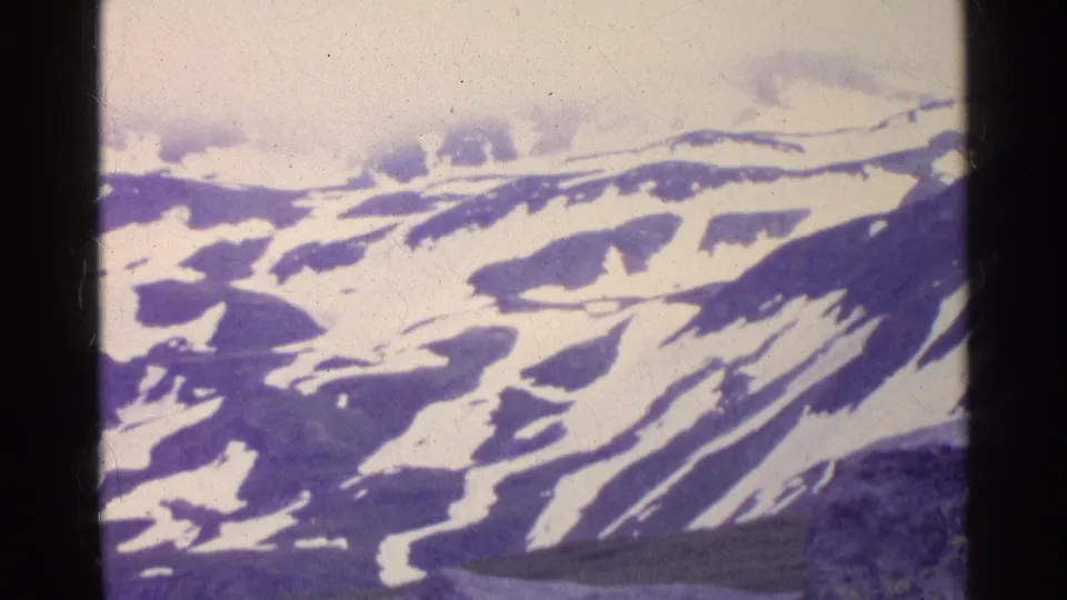 Aerial 8mm view of Swiss alpine ridges with irregular snowfields and soft mid-century color cast.