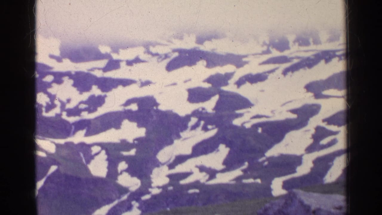 Aerial 8mm frame from Switzerland showing snow-streaked alpine ridges beneath pale haze.