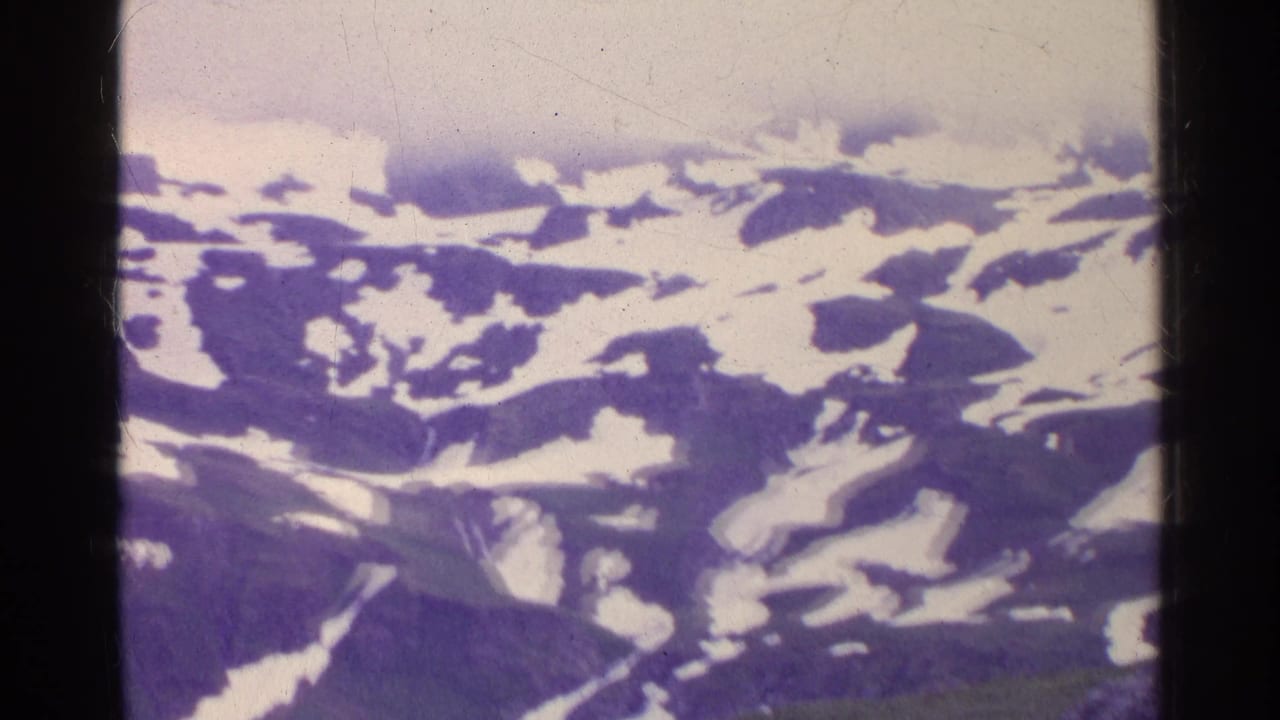 1961 Switzerland 8mm frame showing distant snow patches across dark mountain slopes under low cloud or fog.