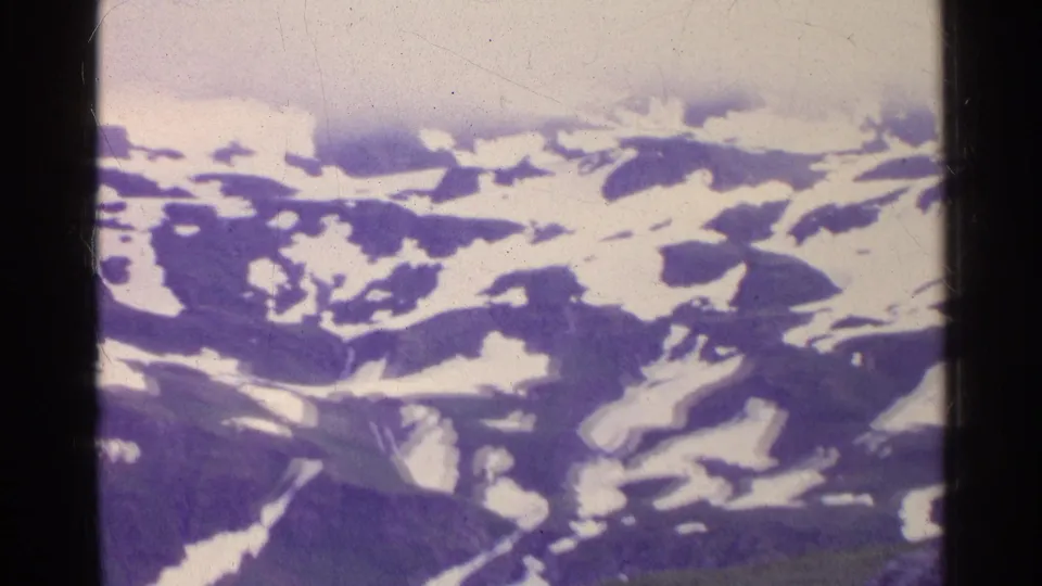 1961 Switzerland 8mm frame showing distant snow patches across dark mountain slopes under low cloud or fog.