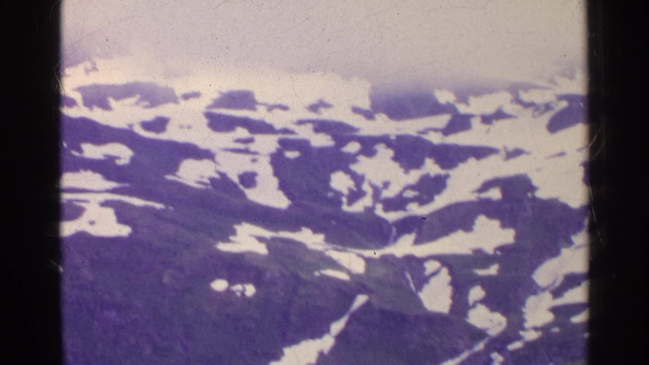 1961 Switzerland home-movie frame with snow-covered alpine ridges and purple-blue shadowed slopes beneath fog.