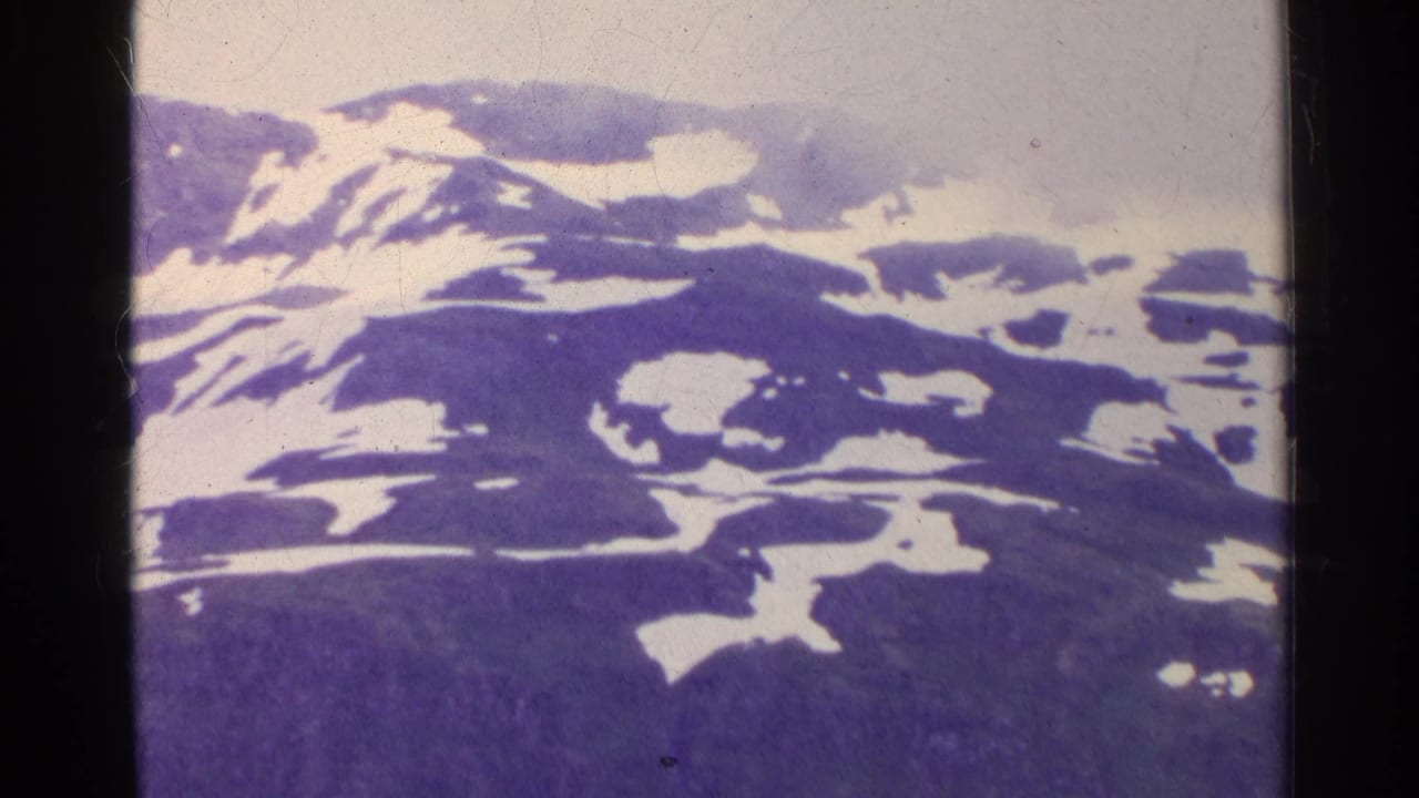 1961 Switzerland frame showing rugged mountain terrain with scattered snow and a foggy, overcast sky.