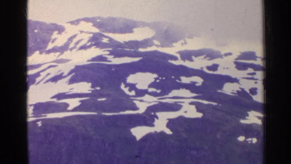 1961 Switzerland frame showing rugged mountain terrain with scattered snow and a foggy, overcast sky.