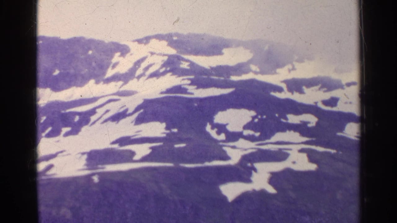 1961 Switzerland 8mm frame showing a distant rocky mountain ridge with scattered snow patches and purple-tinted film color.