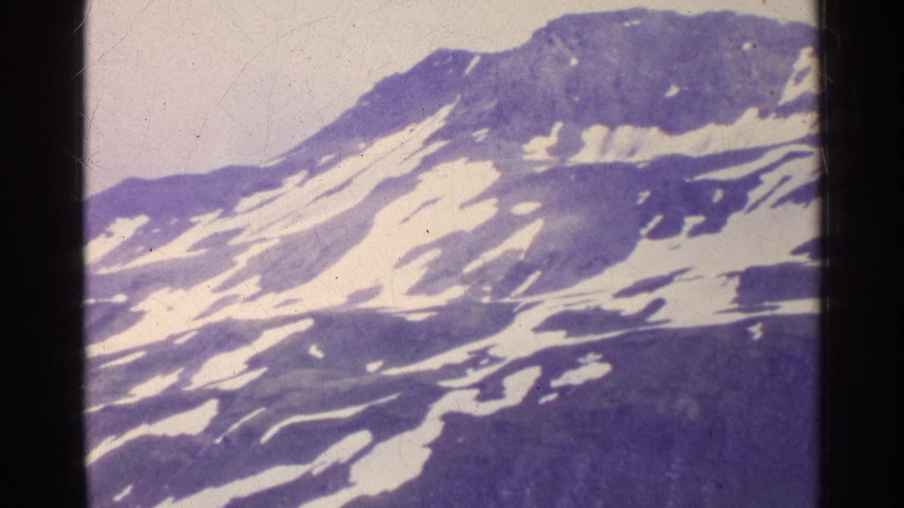 1961 Switzerland 8mm frame showing a snow-streaked mountain slope and ridge, framed by dark film edges and purple color aging.