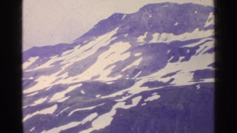 1961 Switzerland 8mm frame showing a snow-streaked mountain slope and ridge, framed by dark film edges and purple color aging.