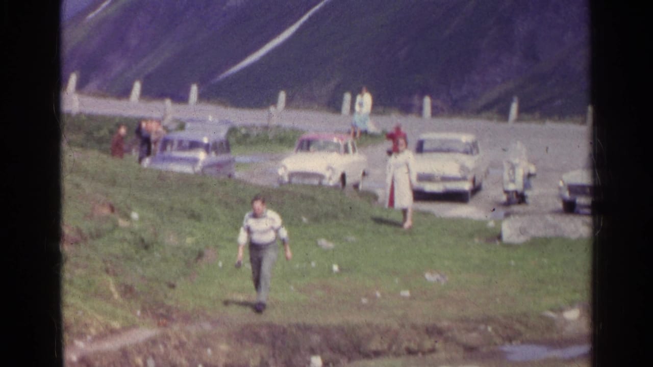 A man in a striped sweater continues away from the roadside group, with a woman in white and parked cars behind him in Switzerland.