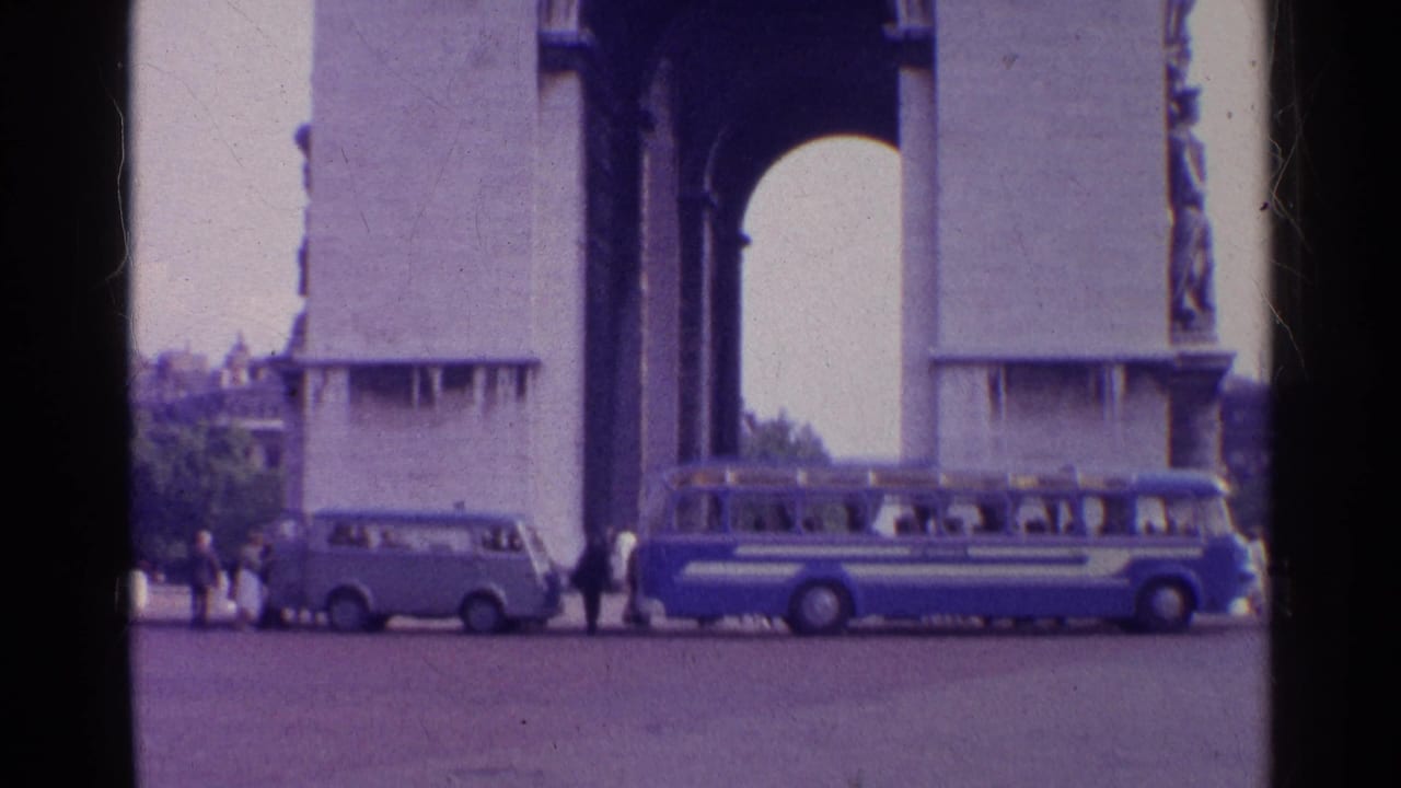 1961 Switzerland home-movie frame showing a monumental stone arch with a blue tour bus, light van, and visitors in the paved foreground.