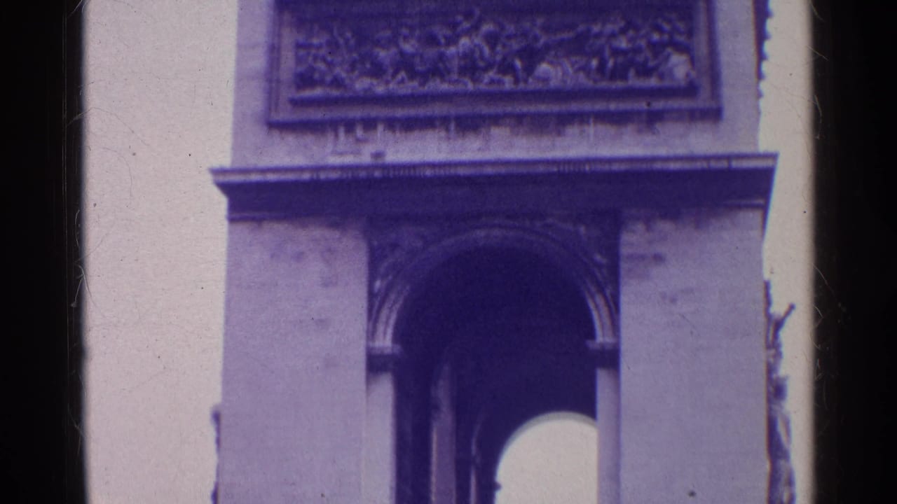 1960s 8mm travel frame showing a close view of a monumental arch facade with relief sculpture, cornice, and dark arch opening.