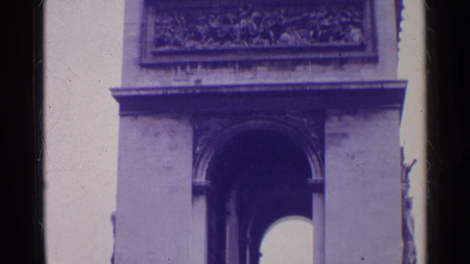 1960s 8mm travel frame showing a close view of a monumental arch facade with relief sculpture, cornice, and dark arch opening.