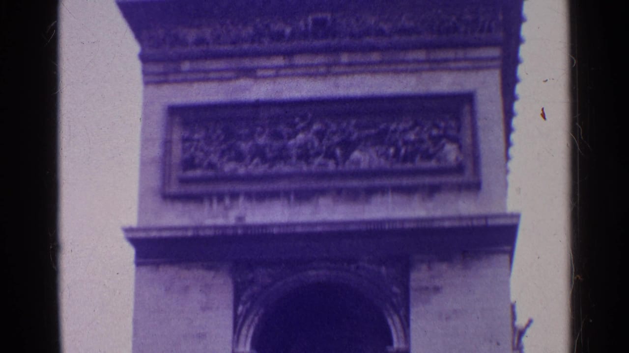 Close 8mm frame of a monumental arch facade, with a rectangular carved panel above the arch and visible aged-film borders.