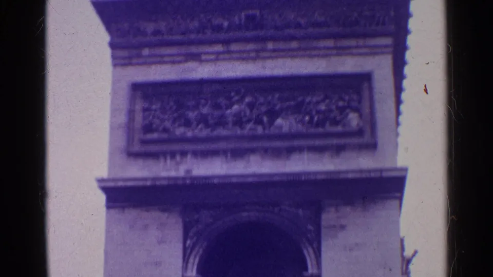 Close 8mm frame of a monumental arch facade, with a rectangular carved panel above the arch and visible aged-film borders.